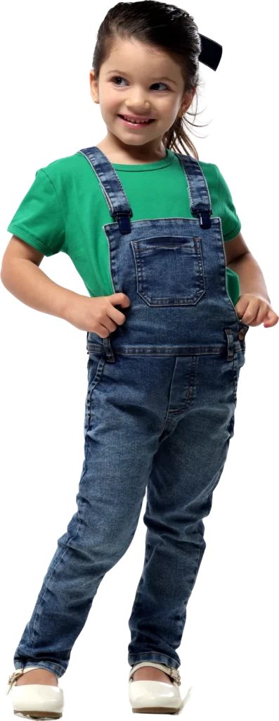 Menina pequena de macacão jeans e camiseta verde sorrindo com as mãos na cintura